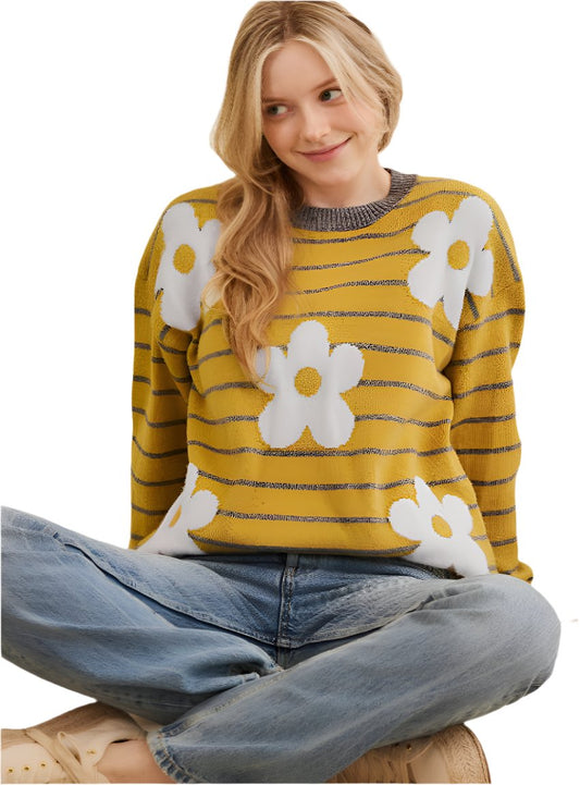 Woman wearing a mustard yellow sweater with white floral design and gray stripes.
