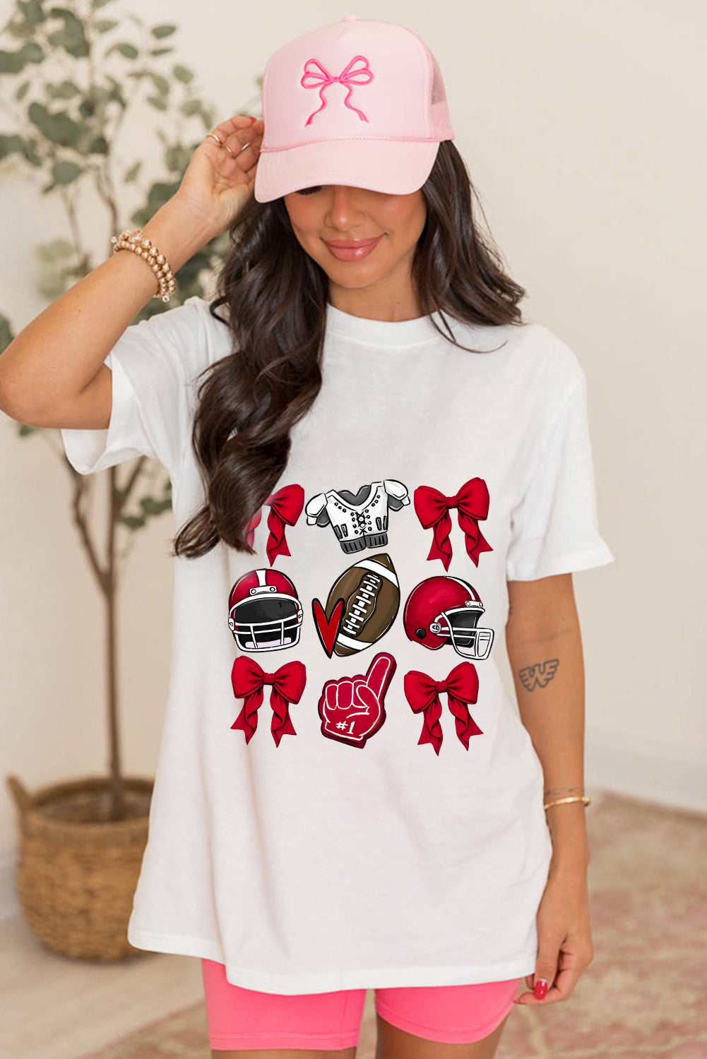 White t-shirt with red football helmets, a football, and bows graphic.