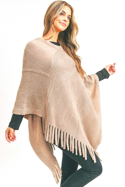 A cozy fringed poncho in tan, draped over a black long-sleeve top and black jeans, perfect for fall.