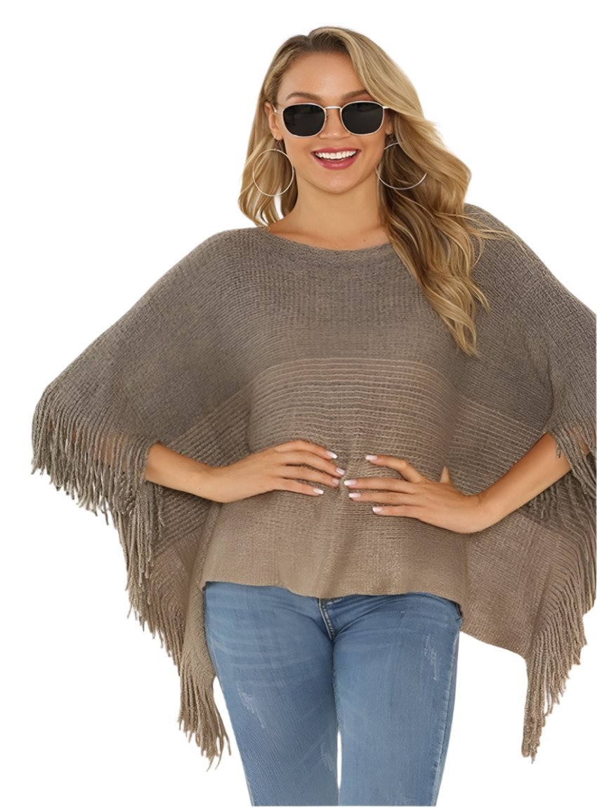 Woman wearing a taupe fringed knit poncho paired with jeans and sunglasses.