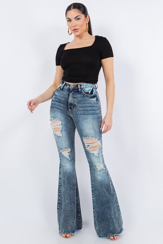 Woman wearing high-rise bell bottom jeans with ripped knee details.
