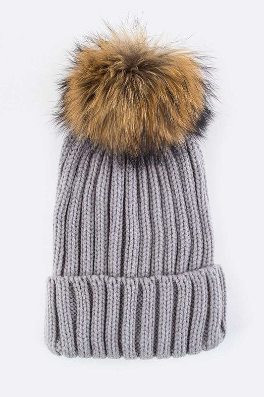 Gray ribbed knit beanie with a faux fur pom, combining comfort and style.
