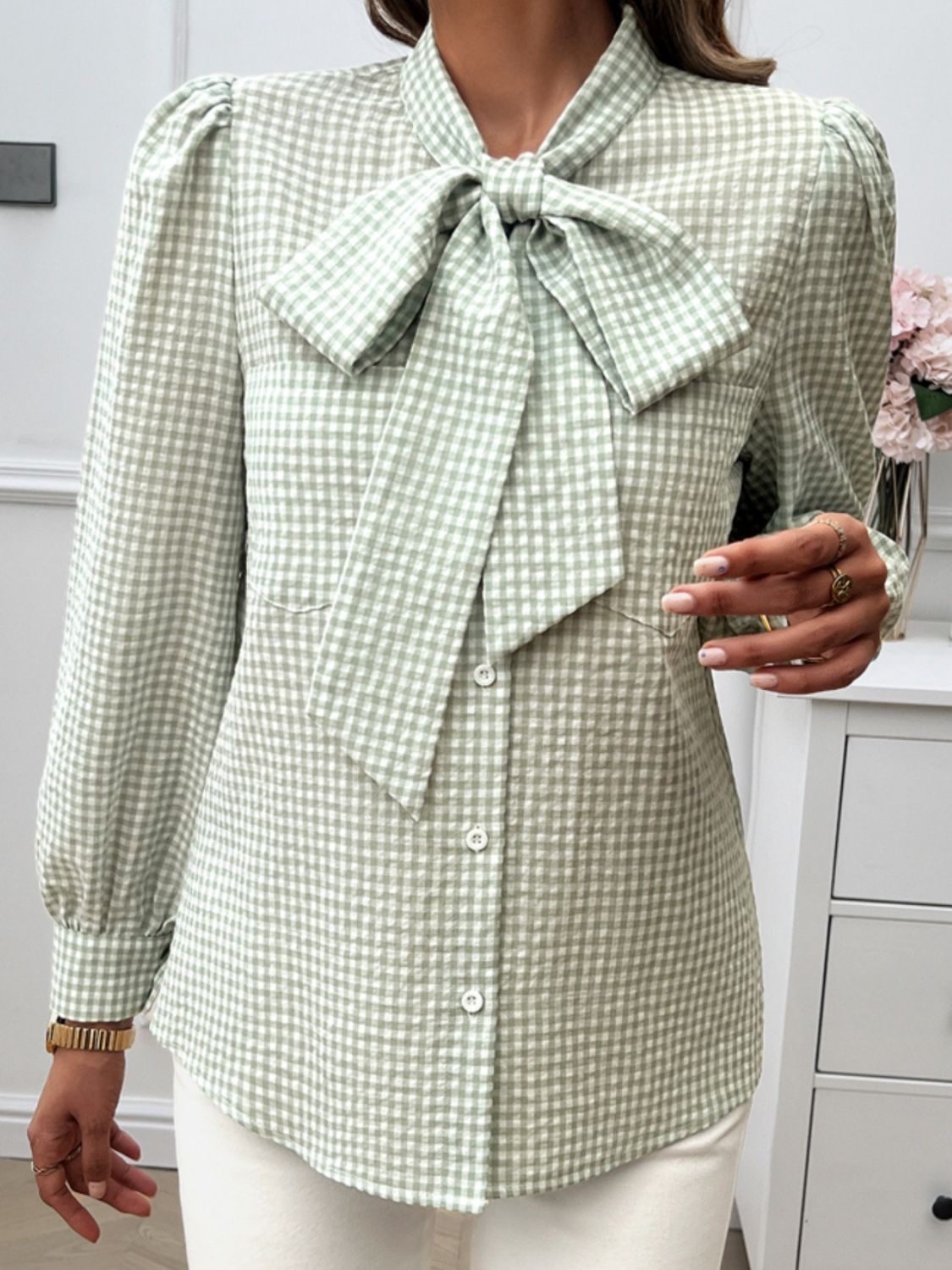 Green gingham blouse with puff sleeves and oversized bow tie detail.
