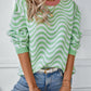 A stylish green striped knit sweater with wavy pattern, paired with light-wash jeans.

