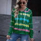 Green tie-dye hooded sweatshirt with multicolored patterns, paired with ripped jeans for a casual look.
