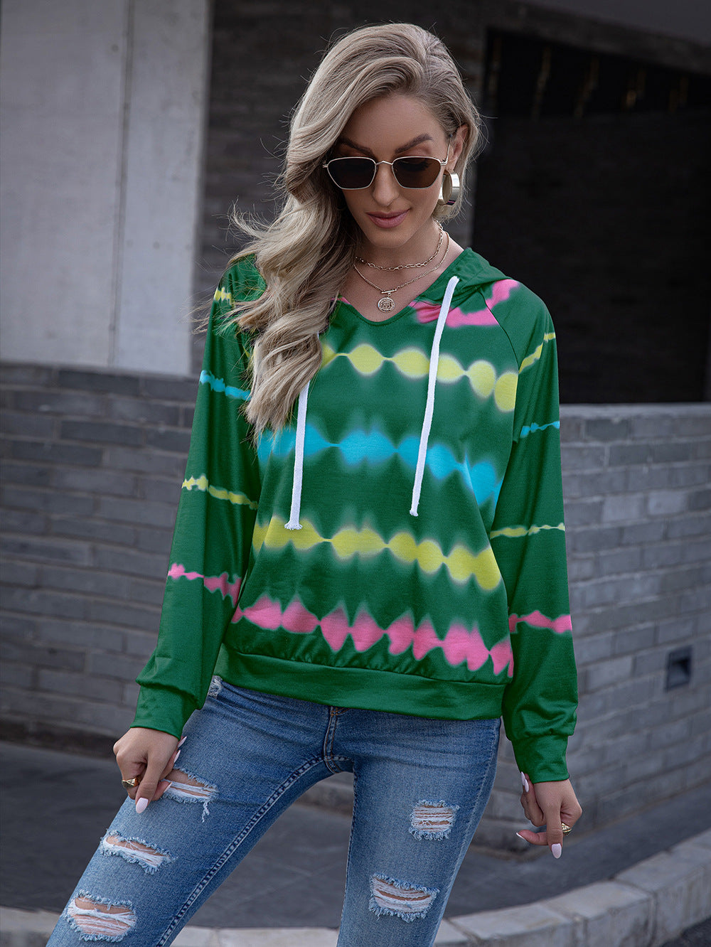 Green tie-dye hooded sweatshirt with multicolored patterns, paired with ripped jeans for a casual look.
