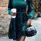 Feminine silhouette of a green velvet dress with puff sleeves and a tiered skirt
