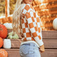 Orange and white checkered sweater with a hood, featuring a front pocket and long sleeves.
