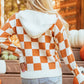 Orange and white checkered sweater with a hood, featuring a front pocket and long sleeves.
