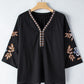 Close-up of floral embroidery on a black boho blouse with relaxed sleeves