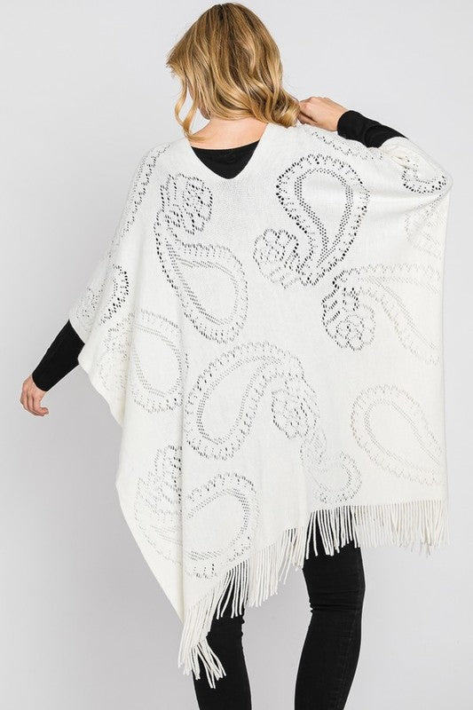 Ivory paisley-pattern knit poncho styled over black outfit.
