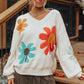 Woman wearing an ivory floral sweater with retro-inspired flower designs.
