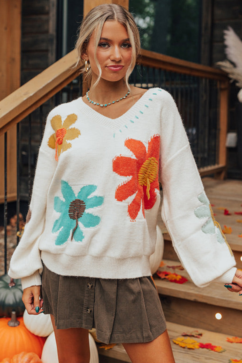 Woman wearing an ivory floral sweater with retro-inspired flower designs.
