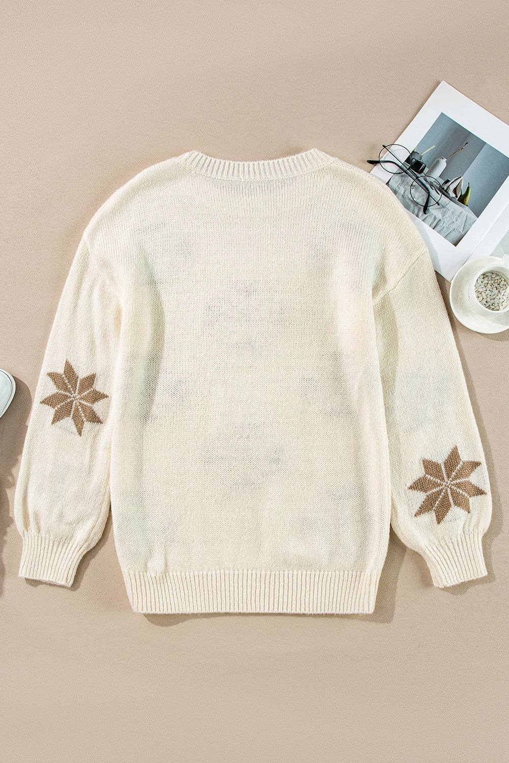 Flat-lay of an ivory knit sweater featuring a snowflake design, ideal for a cozy holiday look.