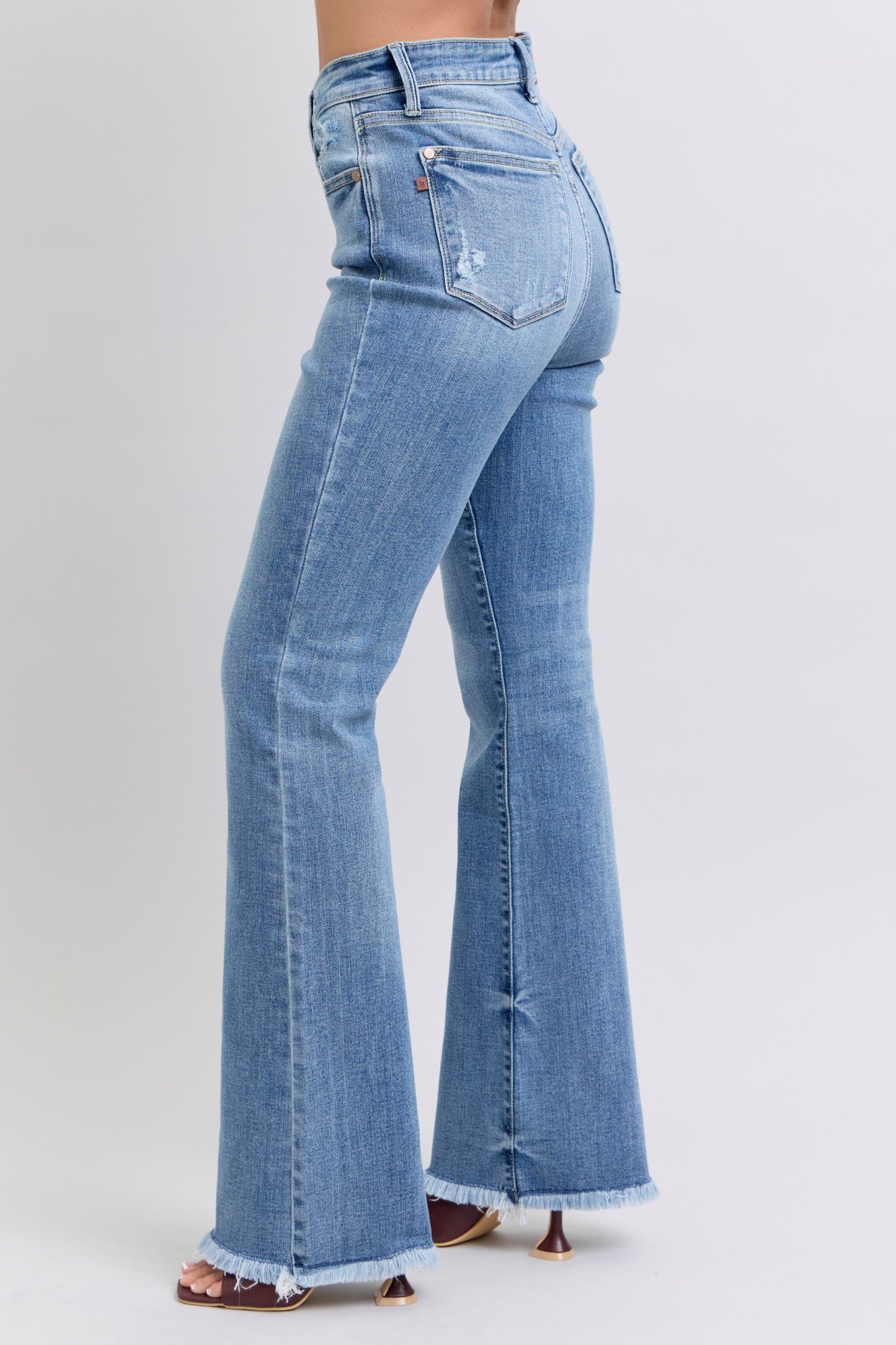 Closeup of waistband on Judy Blue Raw Hem High Rise Bootcut Jeans featuring button and stitch detailing.
