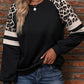 Woman wearing a black sweatshirt with leopard print and white striped sleeve details.
