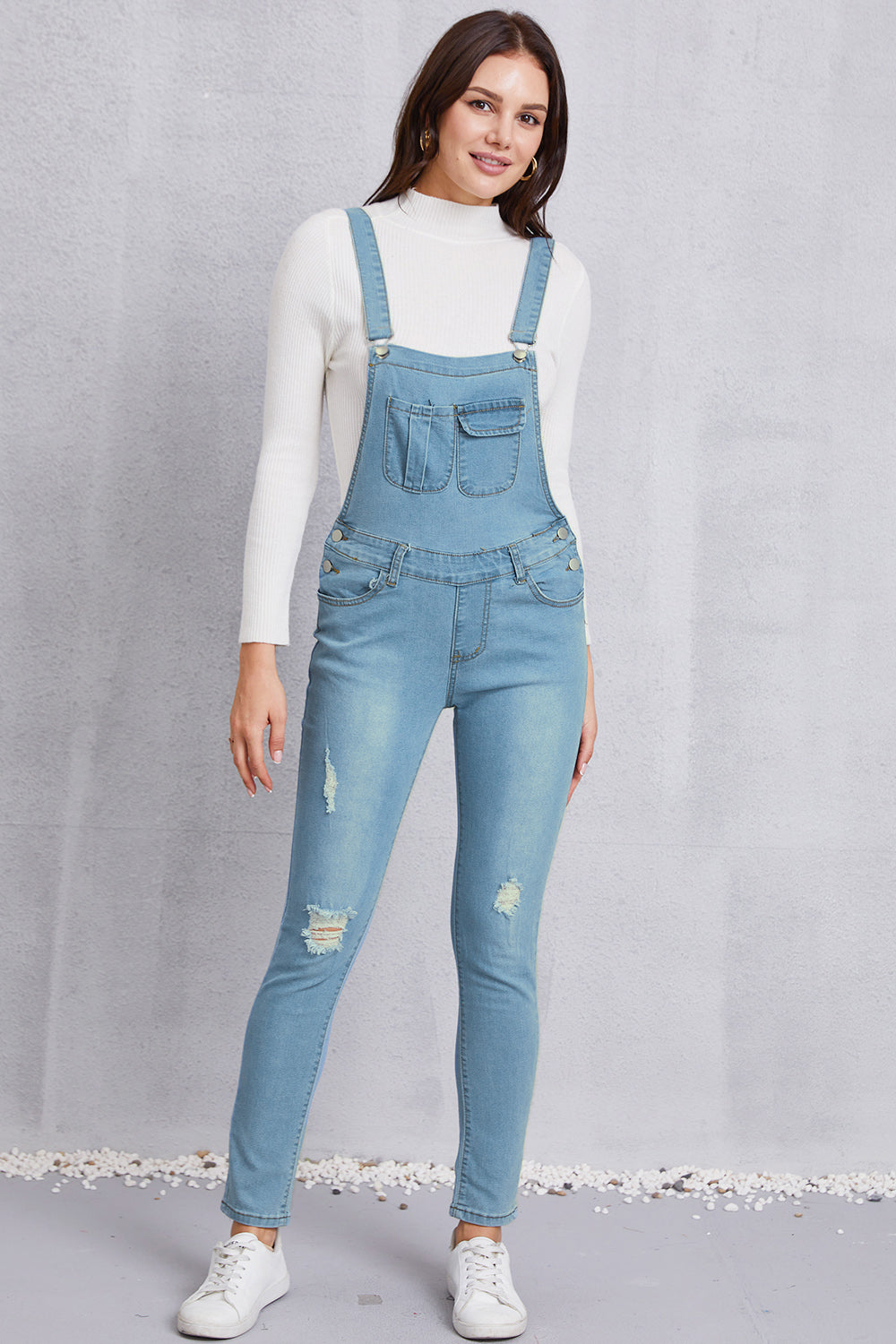 Women’s mid-waist light washed denim overalls featuring distressed accents and slight stretch.
