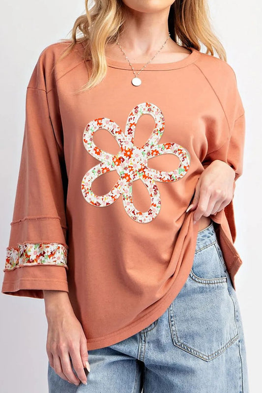 Peach floral applique blouse with round neckline and exposed seam detail, styled with jeans.
