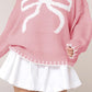 Close-up of a pink knit sweater featuring a large white bow, ideal for winter casual wear.