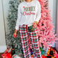 Red and green plaid Christmas pajamas styled with holiday decorations in the background.
