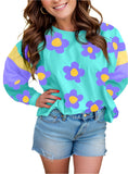 Woman wearing a playful floral long sleeve top with bold purple and yellow flowers on a teal background.
