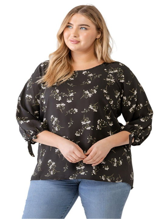 Woman wearing a plus size black blouse with a floral print and tie-sleeve details
