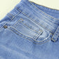 Front view of button fly hem detail ankle-length skinny jeans in dark blue denim with distressing.