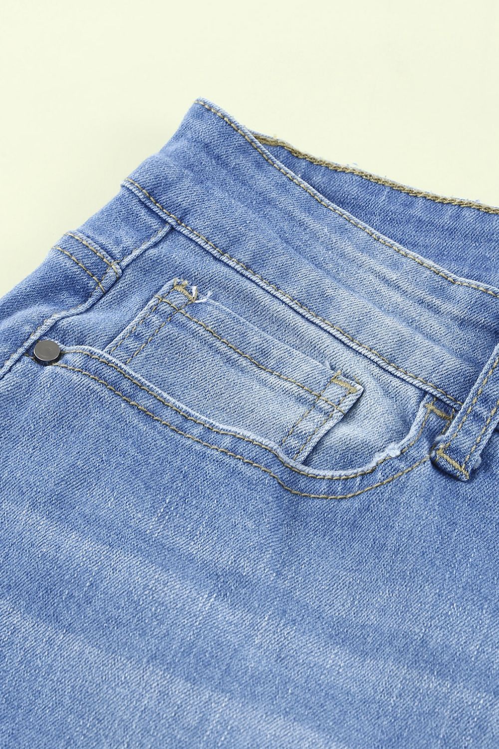 Front view of button fly hem detail ankle-length skinny jeans in dark blue denim with distressing.