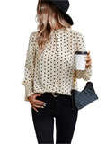 Woman wearing a polka dot ruffled blouse in cream with black dots, paired with black jeans and a quilted bag.
