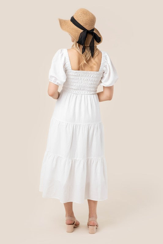 Smocked bodice whimsical white dress with puff sleeves and a square neckline.
