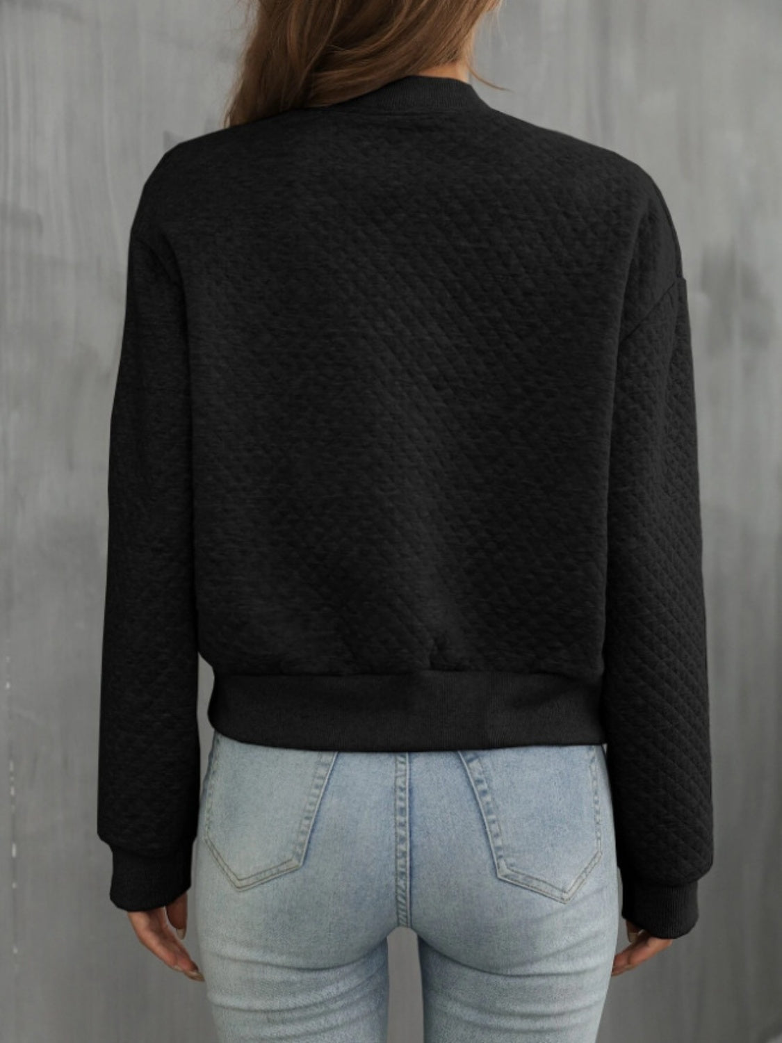 Back view of black quilted bomber jacket with textured quilted details.
