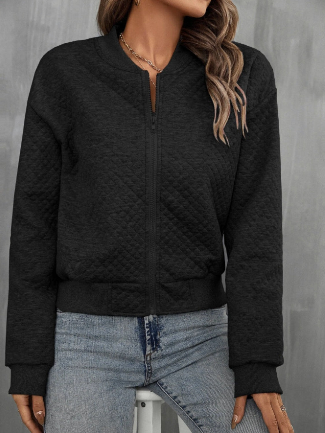 Front view of quilted bomber jacket in black, showing zip-up design and ribbed cuffs.
