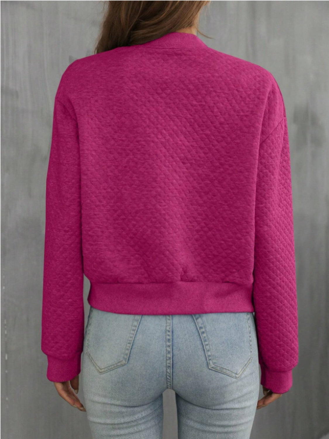 Back view of pink quilted bomber jacket, showcasing quilted fabric and ribbed hem.
