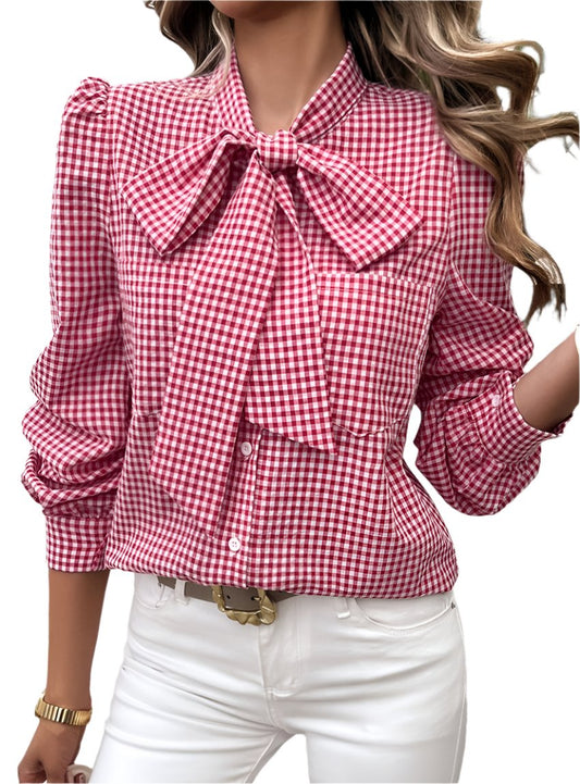 Woman wearing a red gingham bow tie blouse with puff sleeves and white pants.
