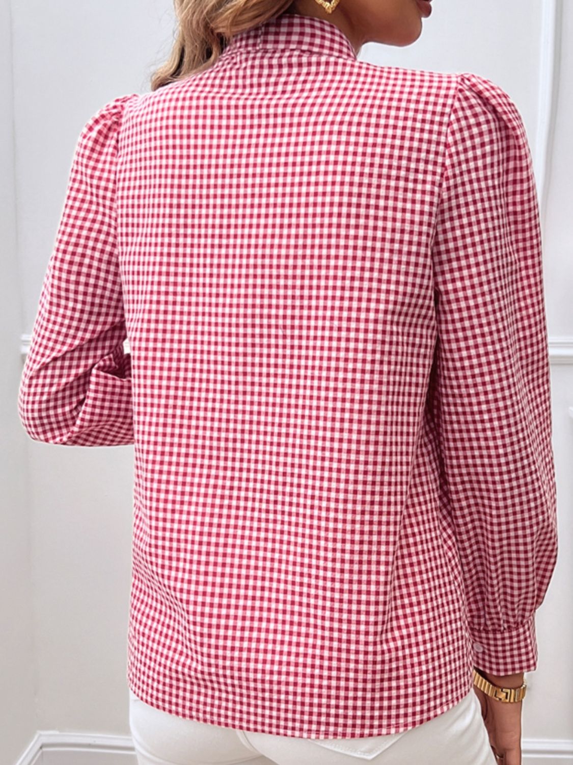 Red gingham button-up blouse with a bow tie and puff sleeves, styled for a casual look.
