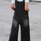 Woman wearing black washed relaxed fit denim overalls with wide straps.
