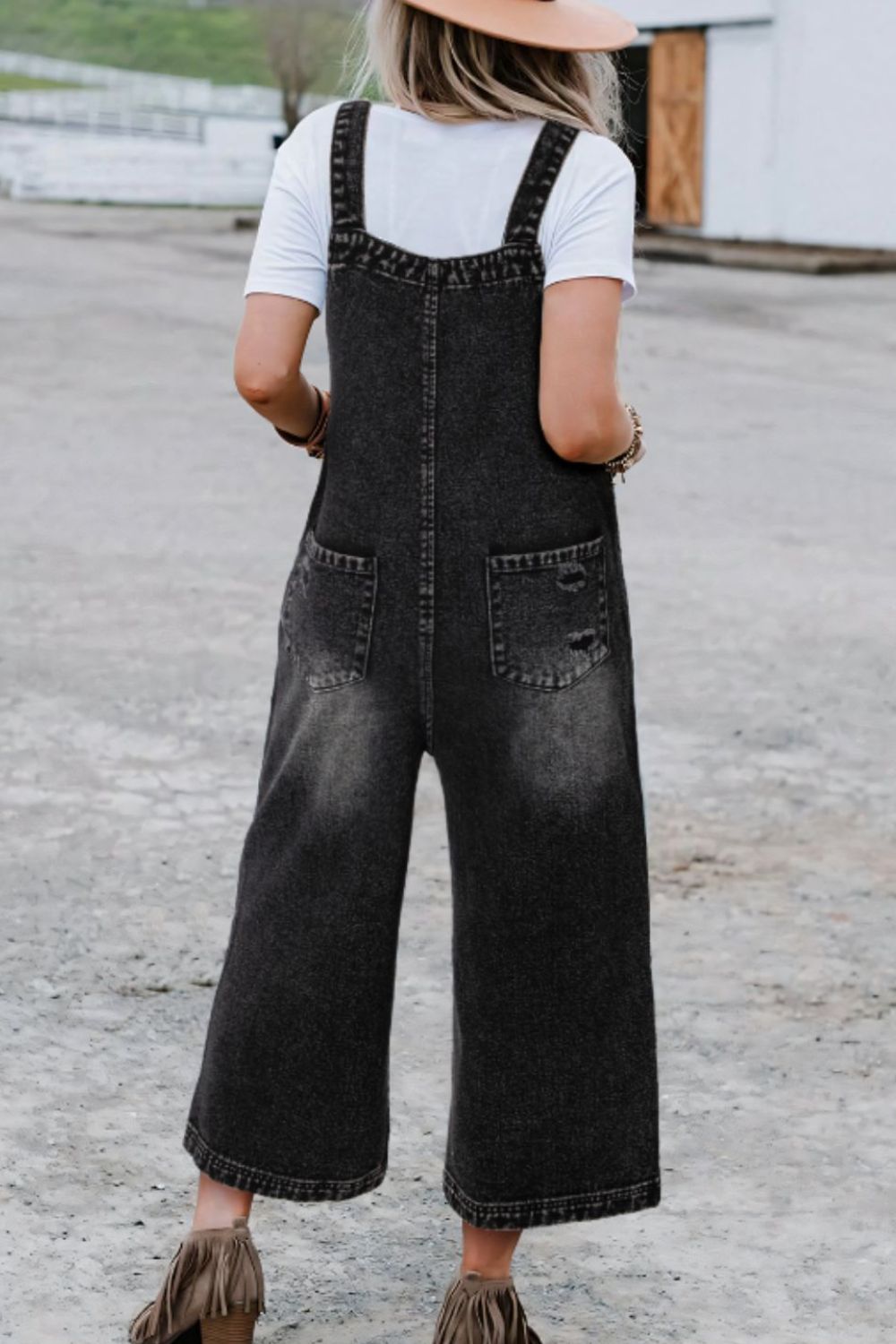 Woman wearing black washed relaxed fit denim overalls with wide straps.
