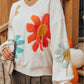 Woman in an ivory sweater with bold flower patterns, styled casually.
