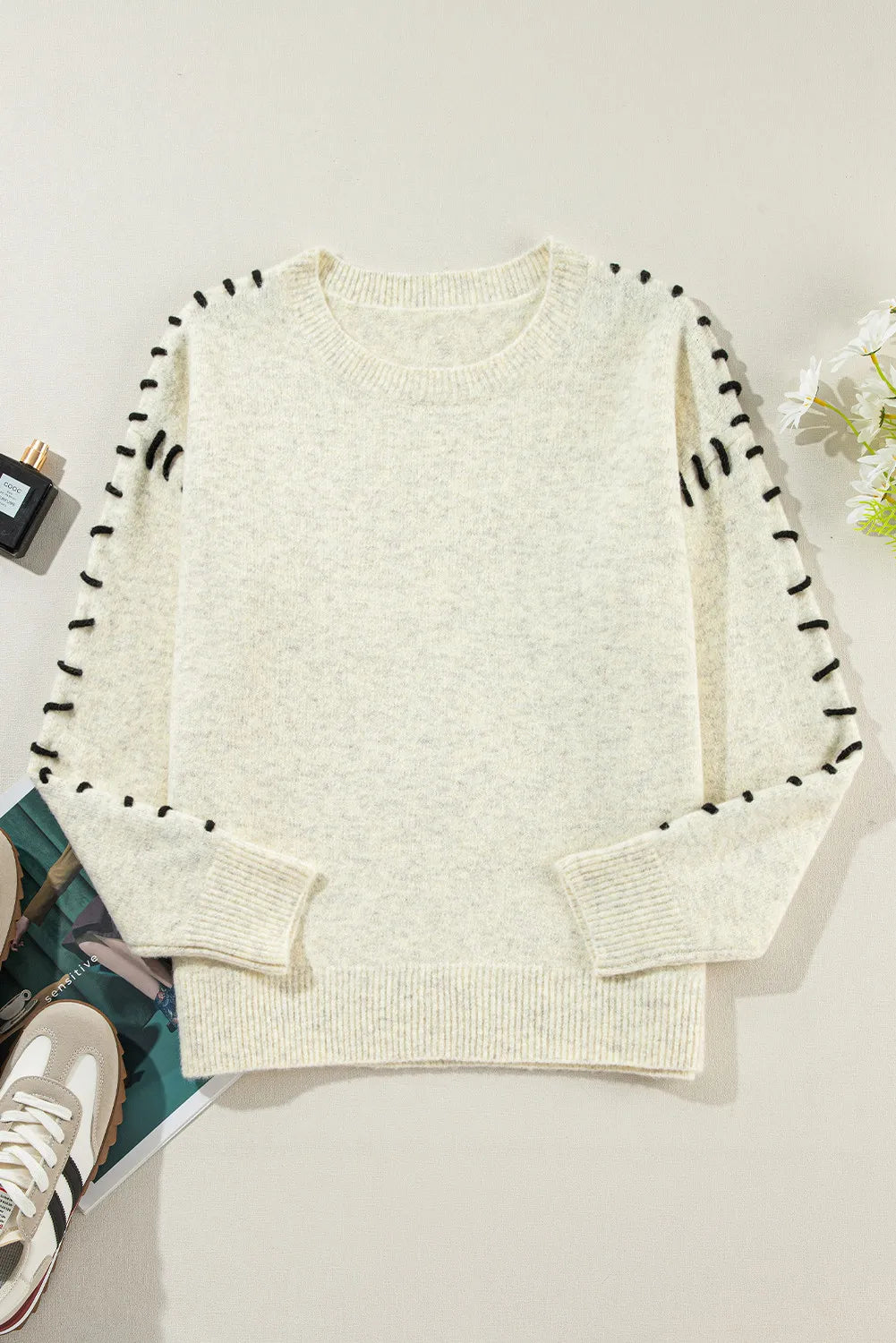 Chic beige sweater with black stitch detailing, adding a touch of contrast.
