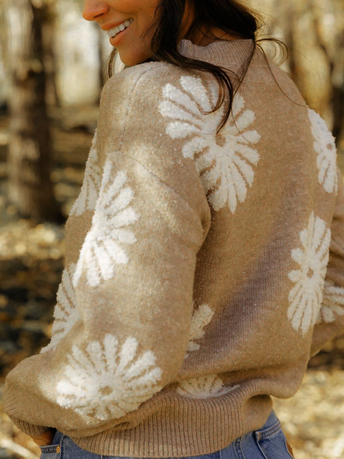 Woman in a beige daisy print sweater, styled casually with denim.
