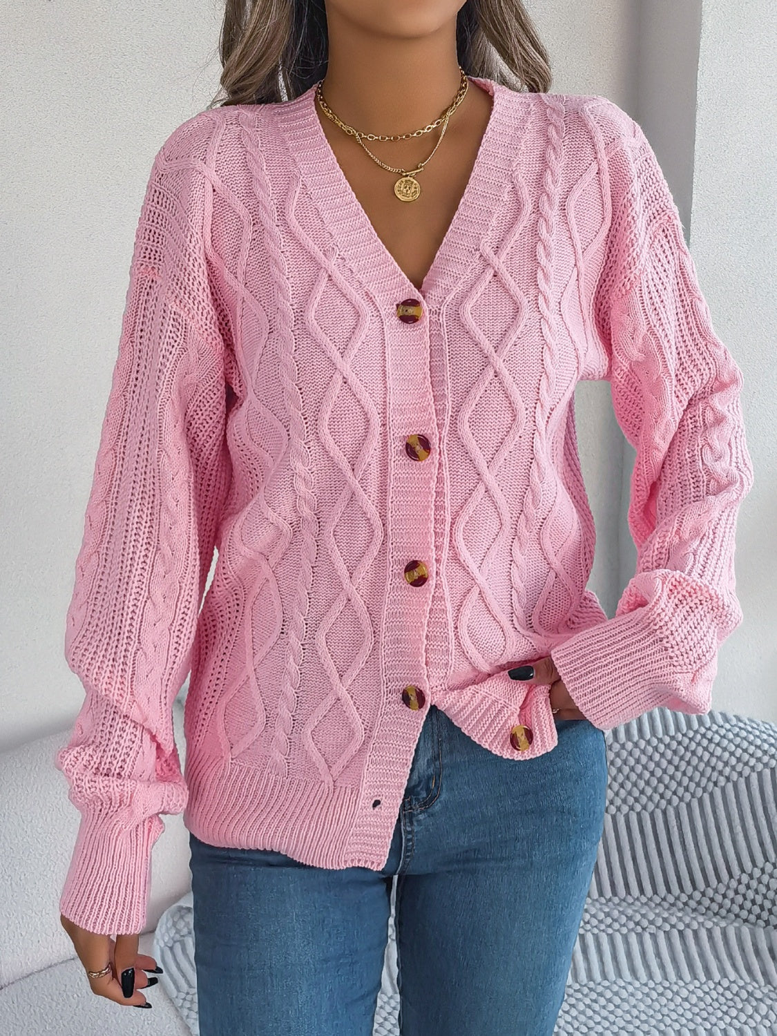 Soft pink cable knit cardigan sweater with tortoiseshell buttons for a chic look.
