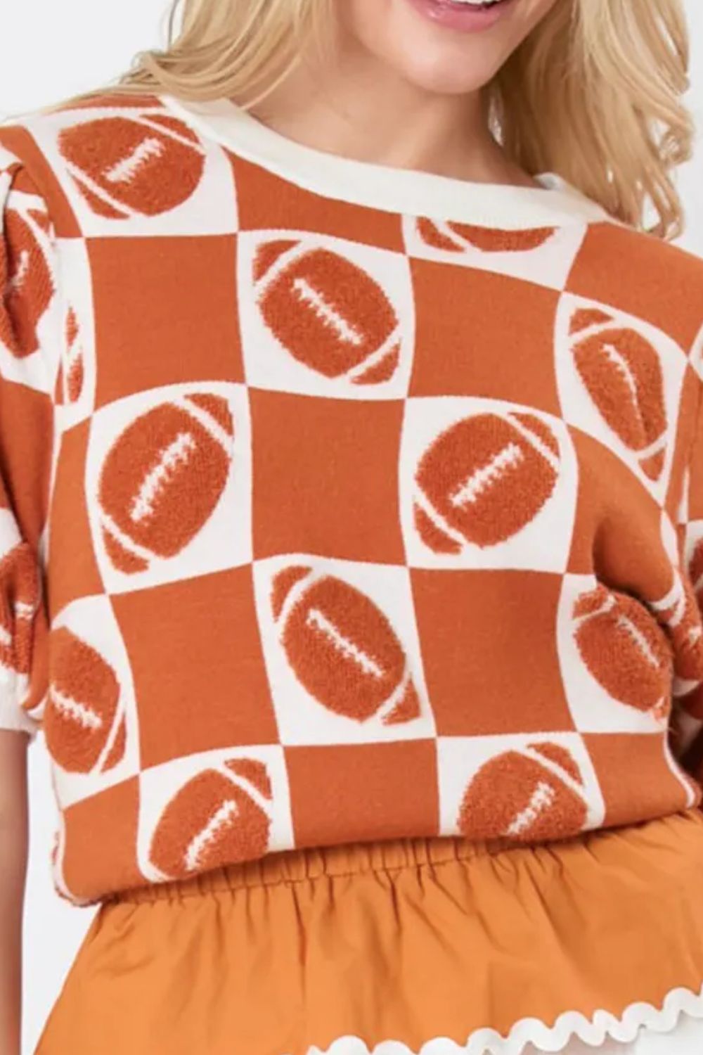 Woman in a stylish orange and white football-themed sweater with short puff sleeves.