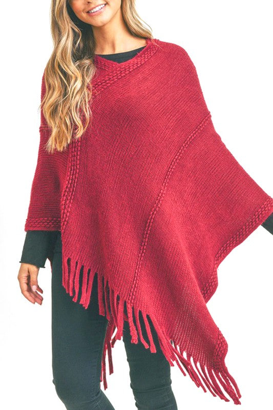 Burgundy fringed poncho paired with black jeans, featuring a textured knit design for a chic and comfortable style.