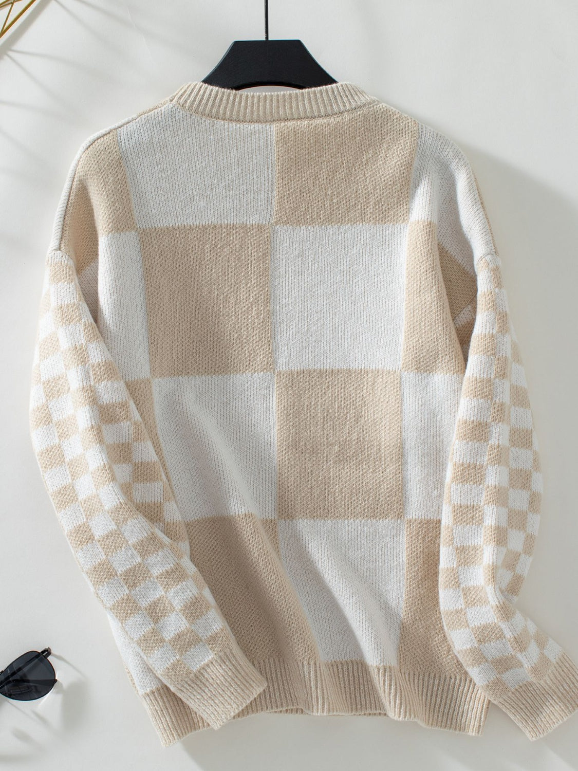 Woman wearing a tan checkerboard patchwork sweater with checkered sleeves.
