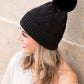 Cozy black knit beanie with faux fur pom and thick knit texture
