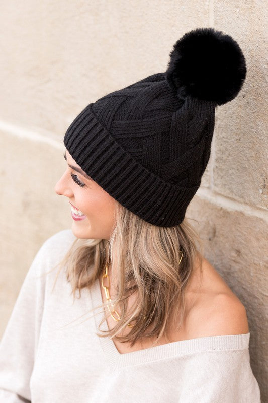 Cozy black knit beanie with faux fur pom and thick knit texture
