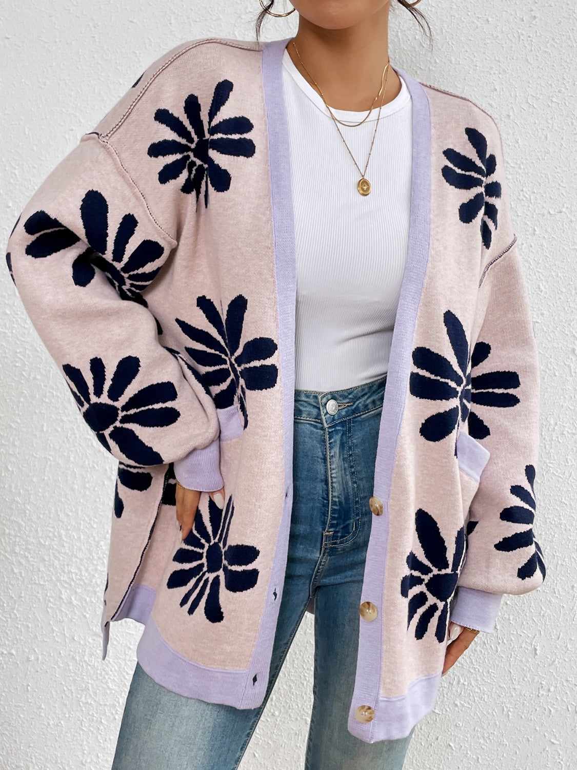 Woman wearing an oversized floral print cardigan in pink with large navy flower designs.
