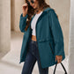 Front view of a turquoise womens rain jacket with waterproof fabric and zippered pockets.
