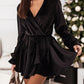 Woman in black velvet tie-waist dress with V-neck and ruffle cuffs.
