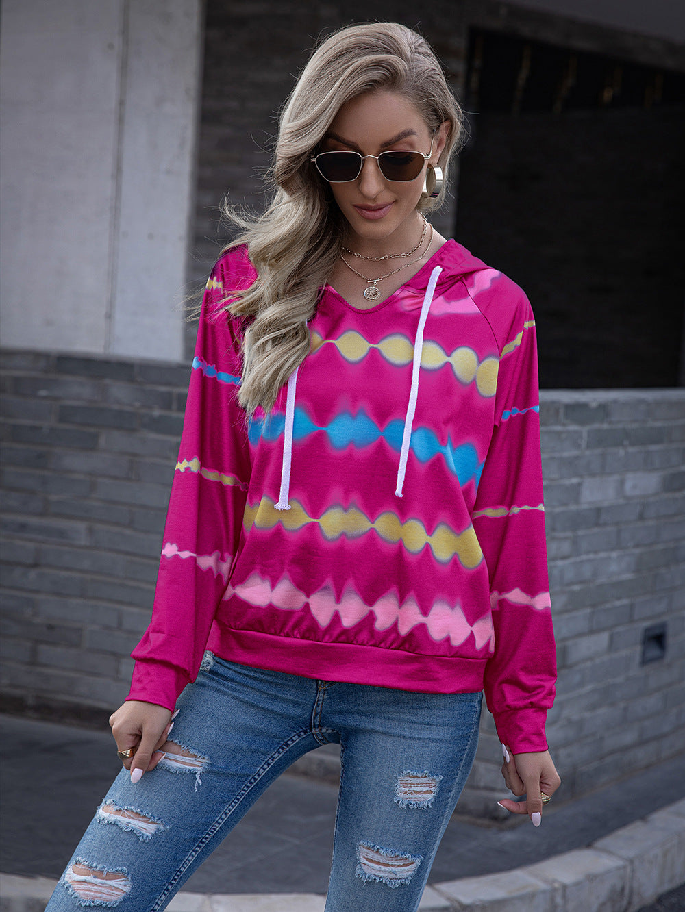 Woman wearing a vibrant pink tie-dye hooded sweatshirt with white drawstrings and raglan sleeves.
